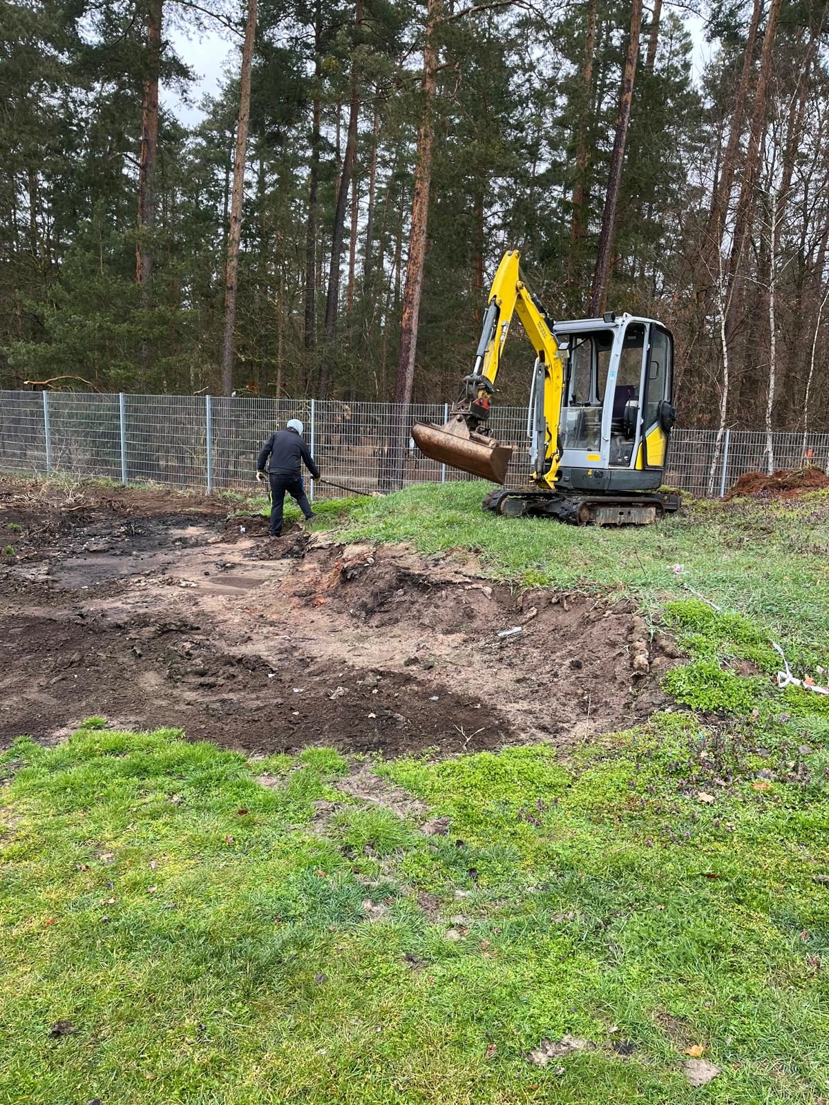 Abgezogene Fläche auf einer Wiese, Minibagger daneben